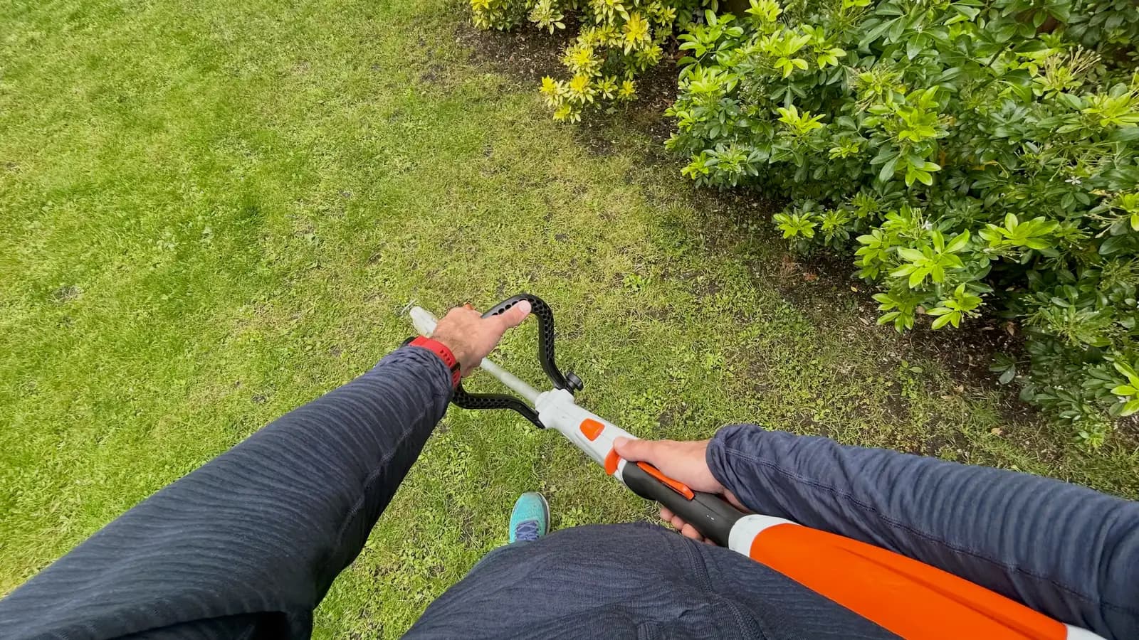 First-person view of hands using a garden tool over grass, an outdoor egocentric capture from a real contributor.